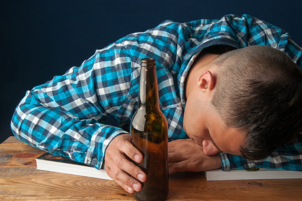 College student asleep on books with beer in hand because of binge drinking.