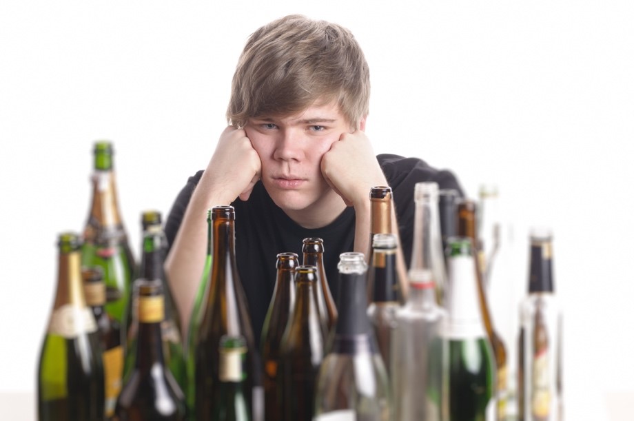 A teenage boy in front of a collection of alcohol bottles.