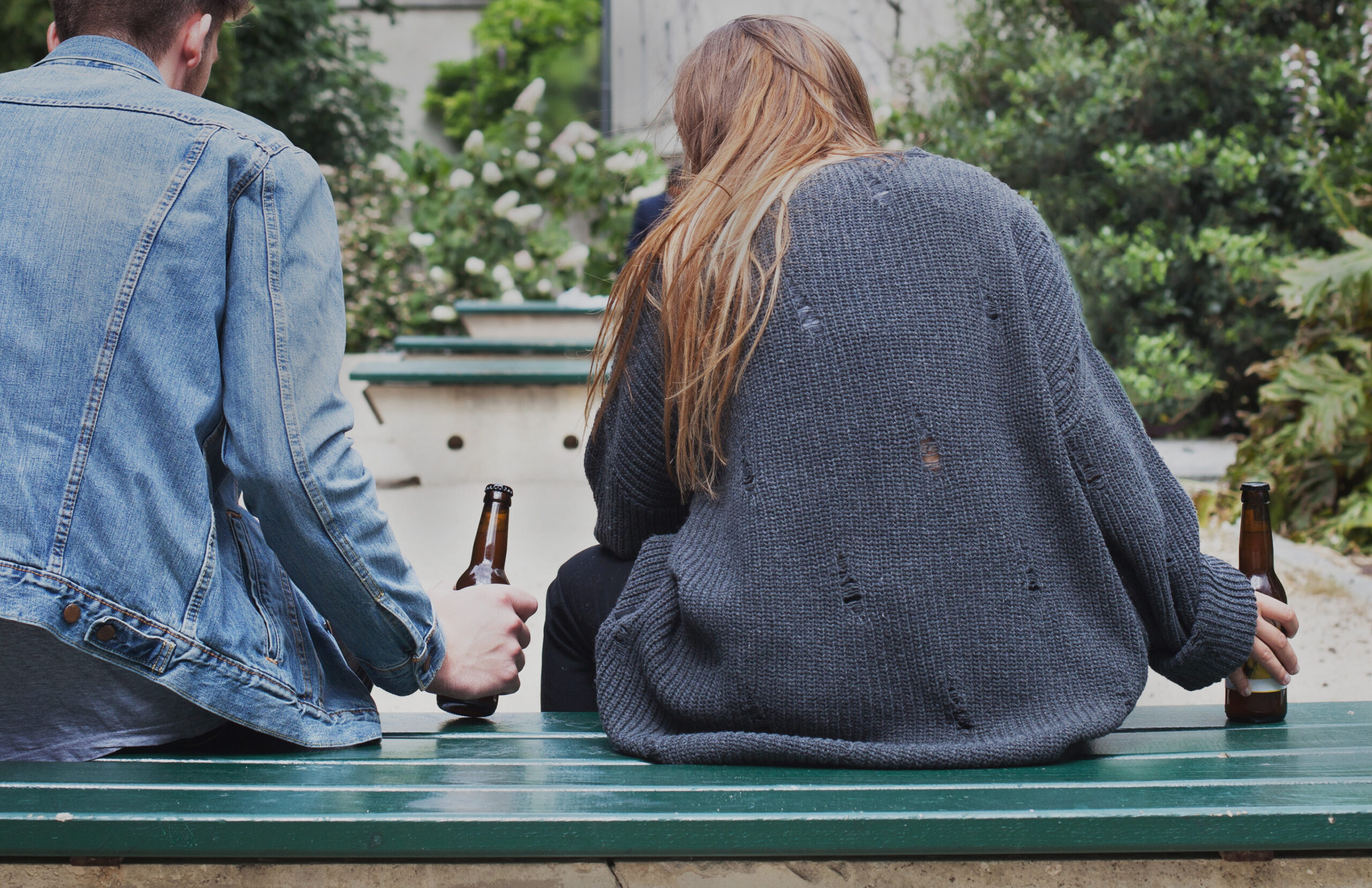 A teenage boy and teenage girl drinking alcohol on a bench.