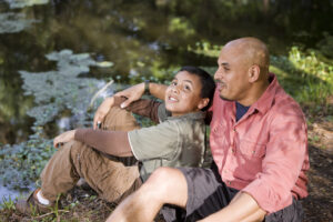 Latinx father speaking to his son by a pond.